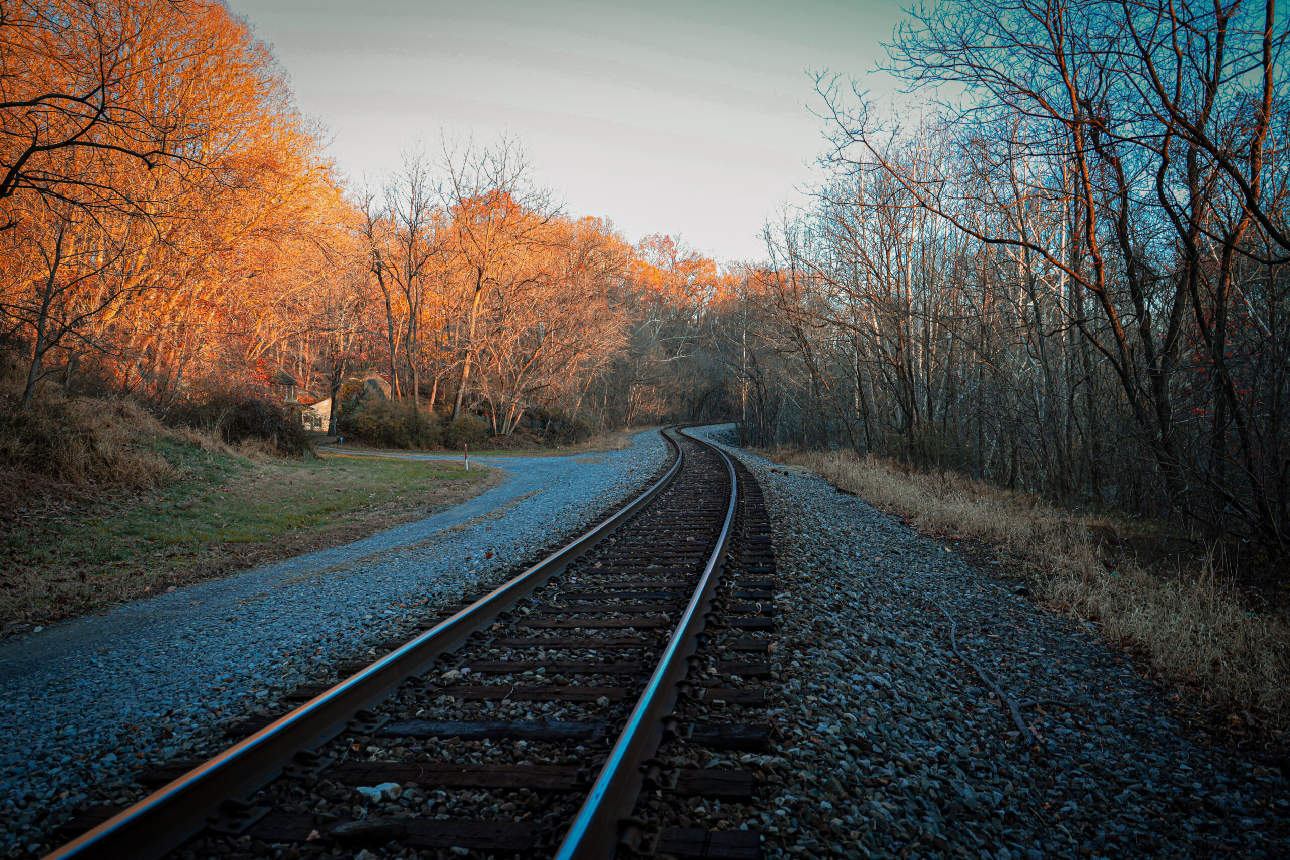 Cinematic landscape of a winding railroad track passing through a forest with autumn foliage and bare winter trees