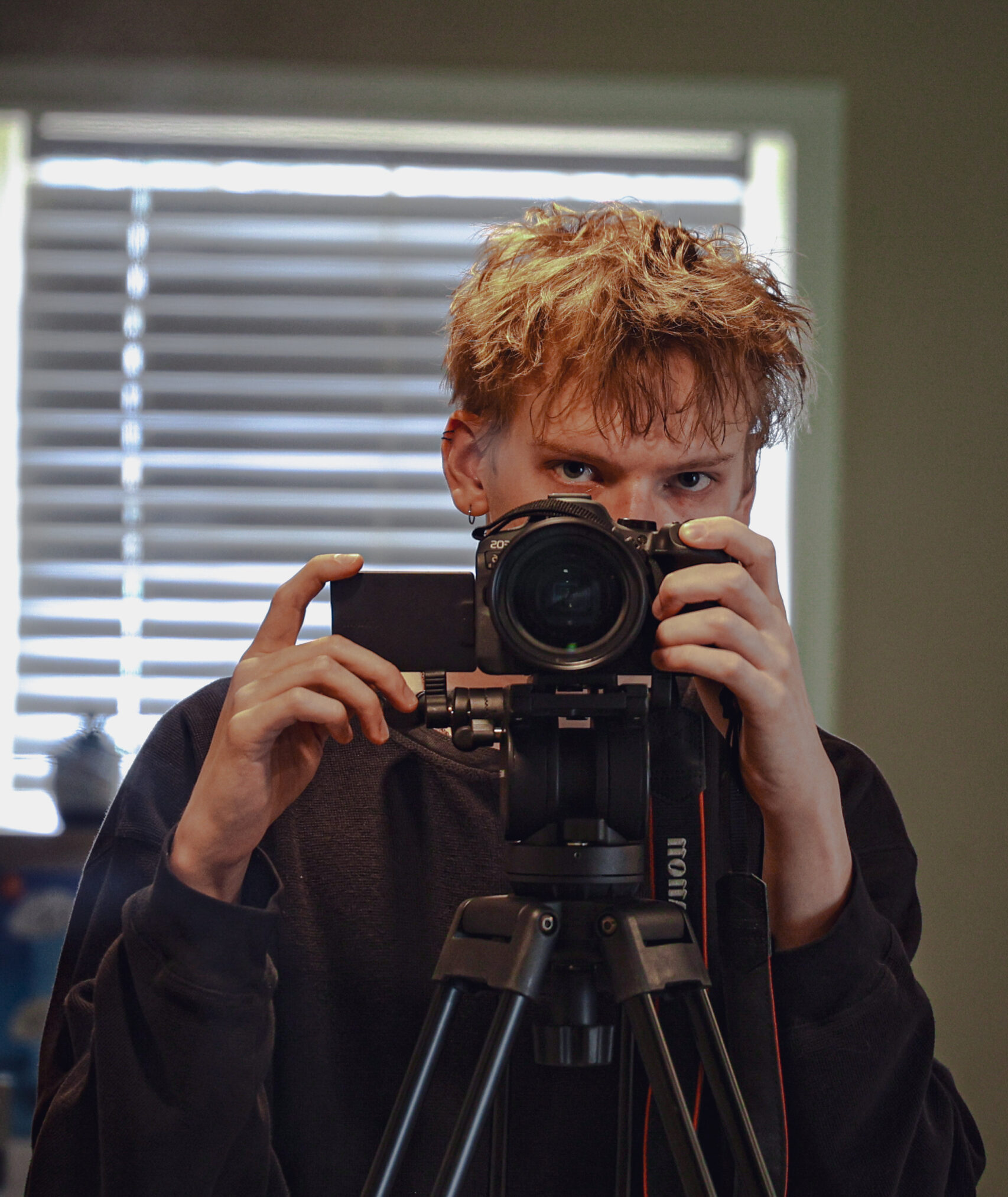 Jake Leese, a professional videographer and visual artist, taking a mirror self-portrait with a DSLR camera mounted on a tripod